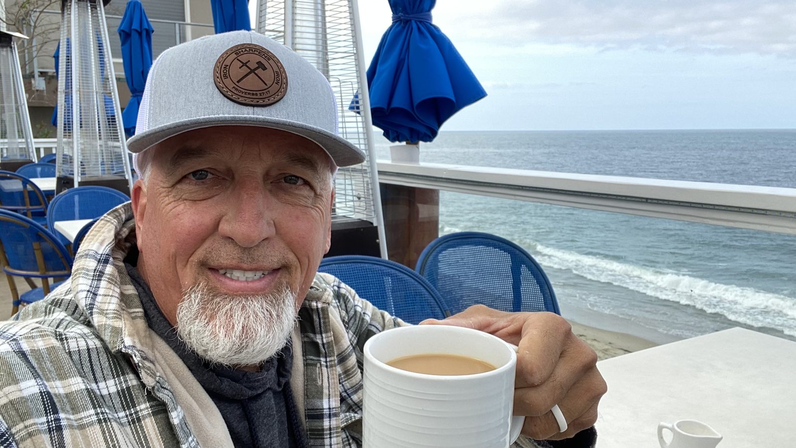 Rick Hopper enjoying coffee by the ocean wearing an Iron Sharpens Iron Proverbs hat